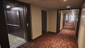 Un pasillo de hotel con alfombra estampada, puertas y un extintor en la pared.