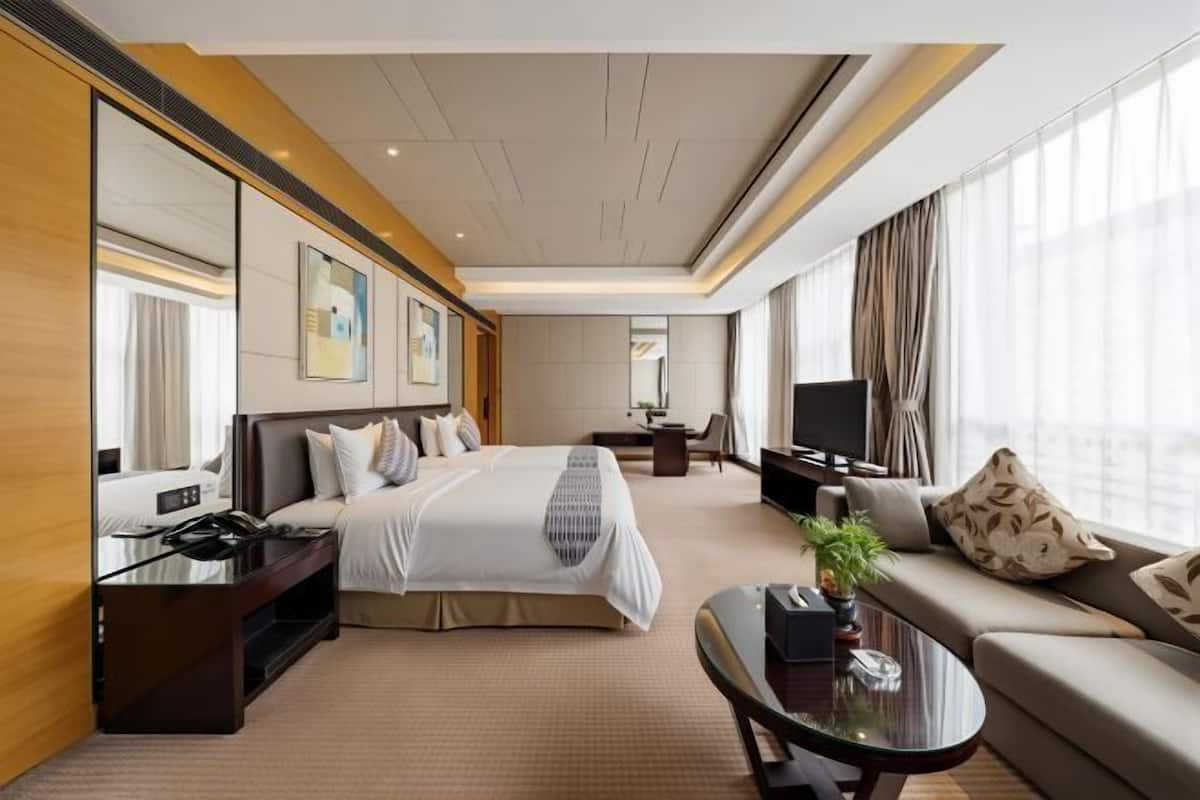 A hotel room with a bed, a sofa, a TV, a desk, and a large window.