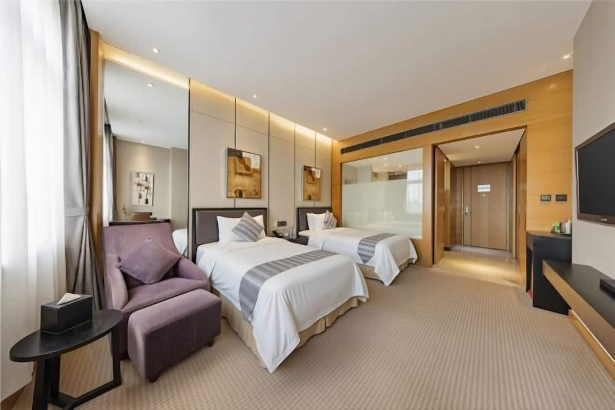 A hotel room with two beds, a sofa, a TV, and a desk.