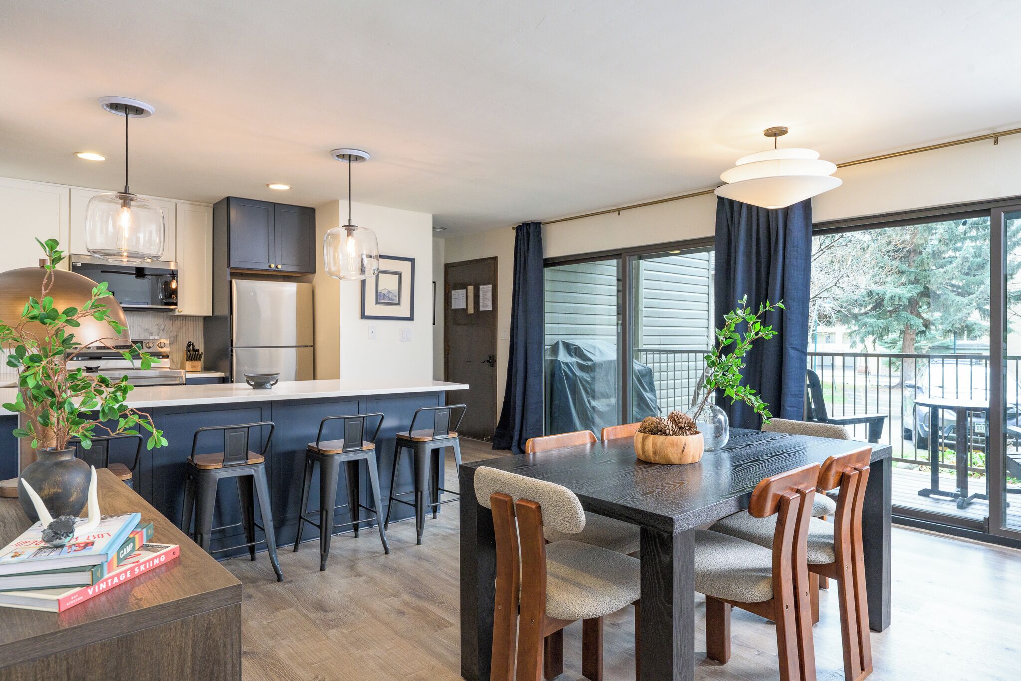 Una cocina moderna con taburetes de bar, una mesa de comedor con sillas y ventanas grandes con cortinas.