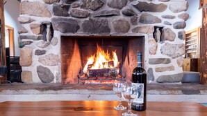 Ein Steinkamin mit Feuer, eine Weinflasche und Gläser auf einem Holztisch.