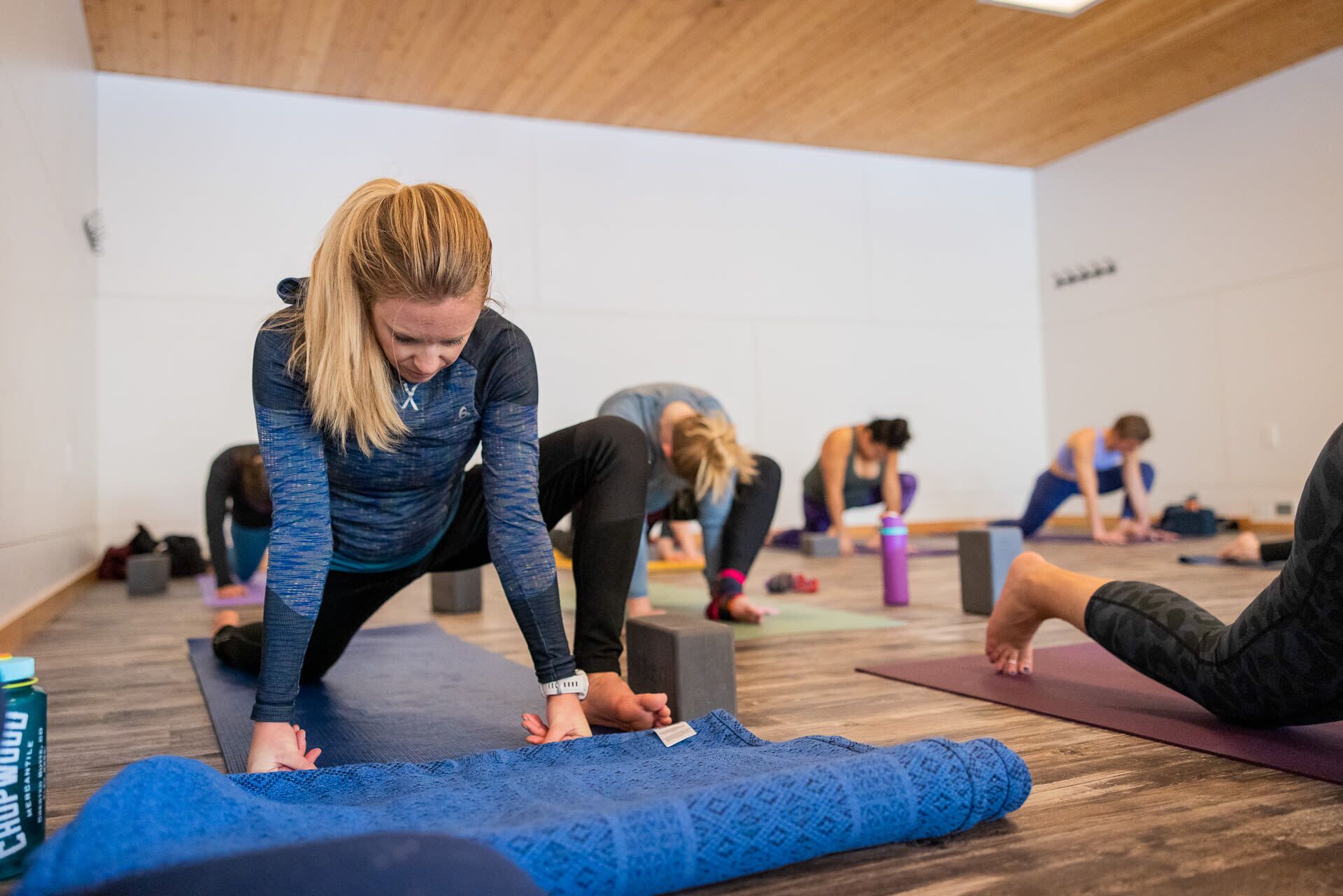 Un grupo de personas en una habitación con suelo de madera y paredes blancas, practicando yoga o estiramientos.