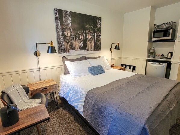 Habitación de hotel con cama, escritorio, silla, un cuadro de lobos y kitchenette.