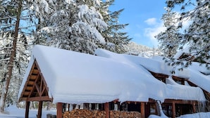 A cabin with a snow-covered roof, wooden beams, and a stack of firewood in front. - Cedar - pet-friendly room at The Inn At Mazama (Mazama)
