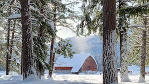 A snow-covered landscape with a rustic barn and a stone building, surrounded by tall trees. - Cedar - pet-friendly room at The Inn At Mazama (Mazama)