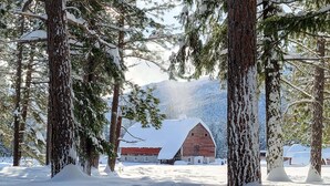 A snow-covered landscape with a rustic barn and a stone building, surrounded by tall trees. - Cedar Plus - large room at The Inn At Mazama (Mazama)