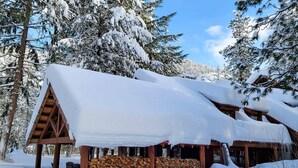 A cabin with a snow-covered roof, wooden beams, and a stack of firewood in front. - Cedar Plus - large room at The Inn At Mazama (Mazama)