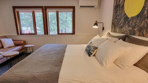 Ein Schlafzimmer mit einem großen Bett, einem Schlafsofa, zwei kleinen Tischen und einem Fenster mit Klimaanlage.