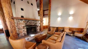 A cozy living room with a stone fireplace, leather sofas, and wooden accents. - Fir - double queen bedroom at The Inn At Mazama (Mazama)
