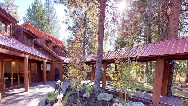 A wooden cabin with a covered patio area, surrounded by trees and a landscaped garden with rocks and small plants. - Fir - double queen bedroom at The Inn At Mazama (Mazama)