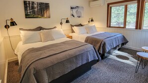 A double room with two beds, a window with a view of trees, a wall-mounted air conditioner, and a painting of a forest scene. - Fir - double queen bedroom at The Inn At Mazama (Mazama)