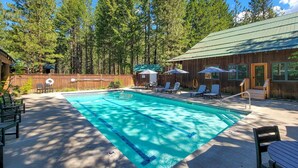 A swimming pool with lounge chairs and umbrellas, surrounded by a wooden fence and tall trees. - Fir - double queen bedroom at The Inn At Mazama (Mazama)