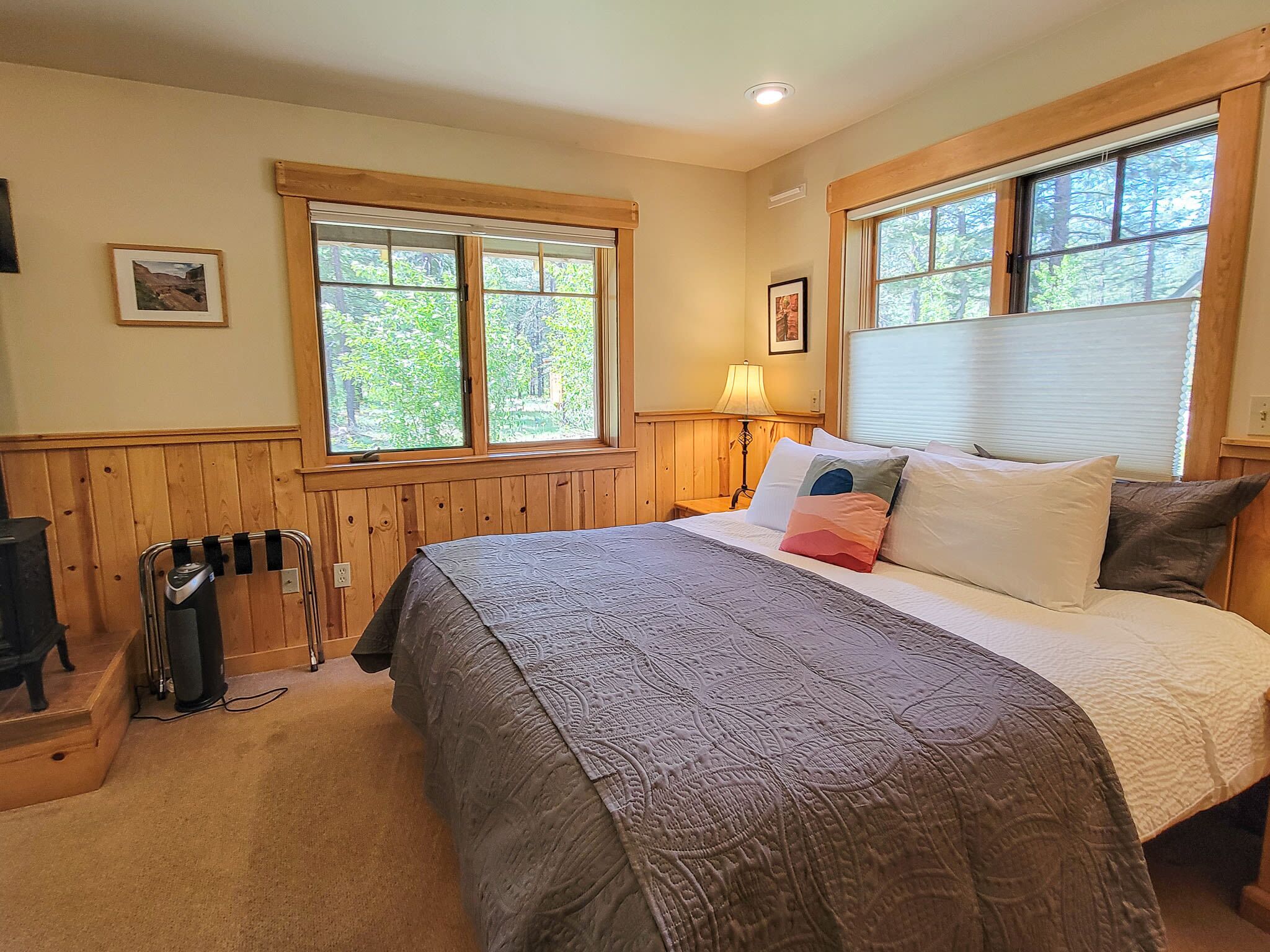 A bedroom with a large bed, two windows with wooden frames, a lamp, and a radiator.