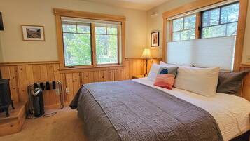A bedroom with a large bed, two windows with wooden frames, a lamp, and a radiator.