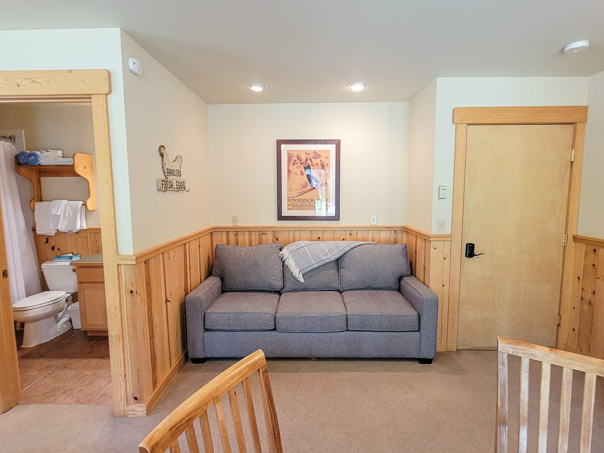 A cozy room with a wooden bench, a grey sofa, a wooden door, and a framed picture on the wall.
