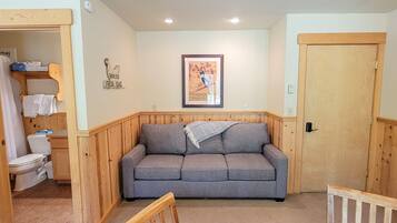 A cozy room with a wooden bench, a grey sofa, a wooden door, and a framed picture on the wall.