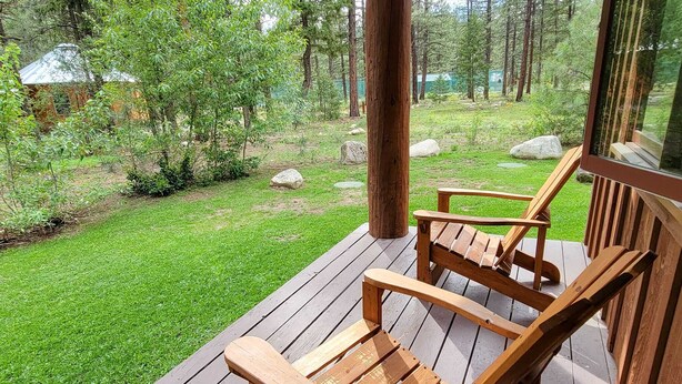 Eine Holzterrasse mit zwei Holzstühlen, umgeben von einer grünen Fläche mit Bäumen und Steinen.