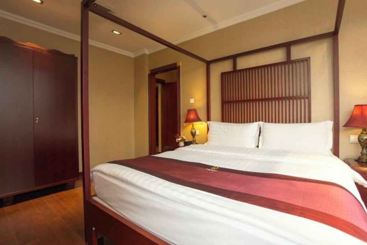 Una habitación de hotel con una cama grande, cabecero de madera, dos lámparas de noche y un armario.