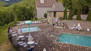 A pool area with lounge chairs and umbrellas, surrounded by a stone wall and greenery.