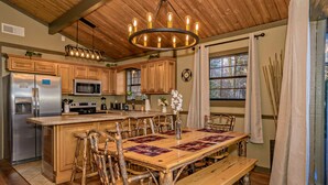 A rustic kitchen with wooden cabinets, a stainless steel refrigerator, a microwave, and a wooden dining table with benches.