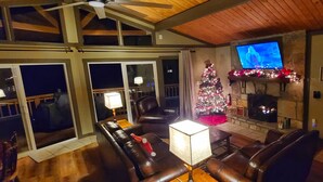 A cozy living room with a fireplace, leather sofas, a television, and a Christmas tree.