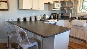 Una cocina con armarios blancos, una isla central con taburetes de bar, una estufa y diversos electrodomésticos.
