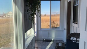 Una habitación soleada con un amplio ventanal, un sofá azul oscuro y una silla de mimbre.