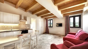 Una cocina moderna con armarios blancos, una isla central y un piso de baldosas hexagonales. En la zona de estar hay un sofá rojo y una ventana con vistas.
