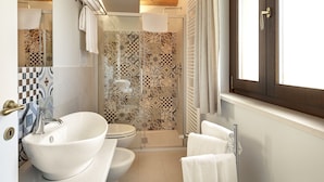 Un baño con un lavamanos grande y blanco, un inodoro, una ducha con azulejos estampados y una ventana con cortinas.
