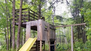 Puinen leikkialue, jossa on liukumäki, metsäisellä alueella.