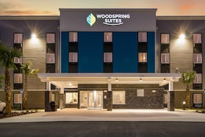 A hotel with a modern facade, a prominent logo, and a number indicating its address. - WoodSpring Suites Jacksonville Baymeadows (Jacksonville)