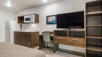 Quarto de hotel compacto com cozinha compacta, uma cama, escrivaninha, cadeira e televisão.