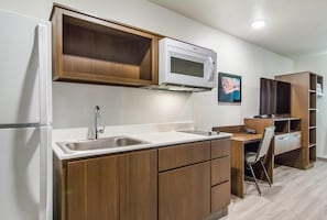 A compact kitchen with a built-in microwave, a sink, and wooden cabinets. - WoodSpring Suites Jacksonville Baymeadows (Jacksonville)