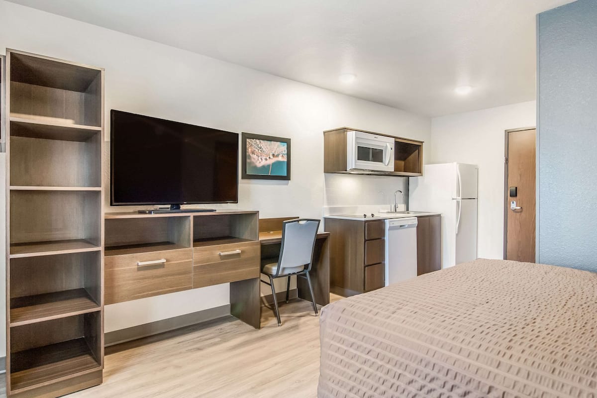 A compact hotel room with a bed, a desk, a chair, a TV, a microwave, and a refrigerator.