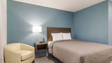 Una habitación de hotel con una cama, una mesita de noche, una lámpara y una silla.