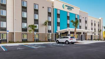 Un hotel a più piani con un cartello che recita 'Woodspring Suites'. Sono visibili posti auto e un'area parcheggio riservata ai disabili.