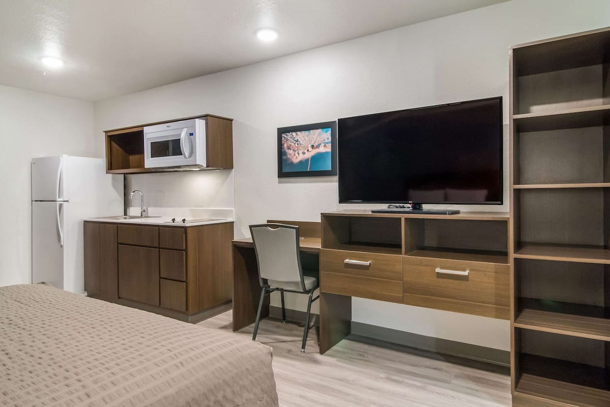A compact room with a kitchenette, a bed, a desk, and a TV.