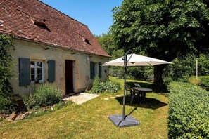 A rustic house with a red-tiled roof, a small garden with a table and chair, and a white umbrella. - Gîte for 4 with bedroom in outbuilding - between Rocamadour and Sarlat (PINSAC)