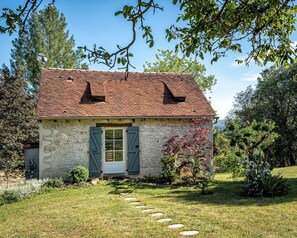 Ein rustikales Steinhaus mit Ziegeldach, einer Holztür und einem Garten mit trittsteinartigen Wegen zum Eingang.