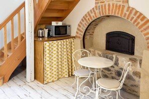 A cozy kitchen with a stone fireplace, a small dining table, and a patterned curtain. - Gîte for 4 with bedroom in outbuilding - between Rocamadour and Sarlat (PINSAC)