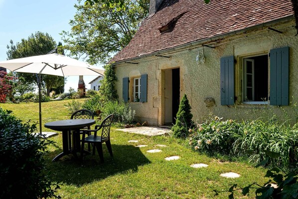 A rustic house with a garden patio featuring a table and chairs. - Gîte for 4 with bedroom in outbuilding - between Rocamadour and Sarlat (PINSAC)