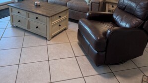 A living room with a brown leather sofa, a matching armchair, a wooden coffee table, and two floor lamps. A painting hangs on the wall above the sofa. - OCEANFRONT 1st floor unit! 150 steps away from the sand AND multiple pools!! (Myrtle Beach)