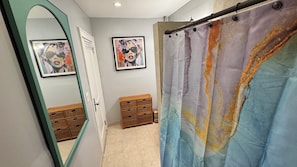 Bathroom features a shower curtain with a marbled design, a wooden storage unit, and a green-framed mirror.