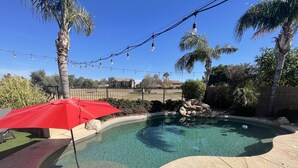 A swimming pool with a red umbrella, surrounded by palm trees and a fence. - Four bedroom home on golf course. (Mesa)