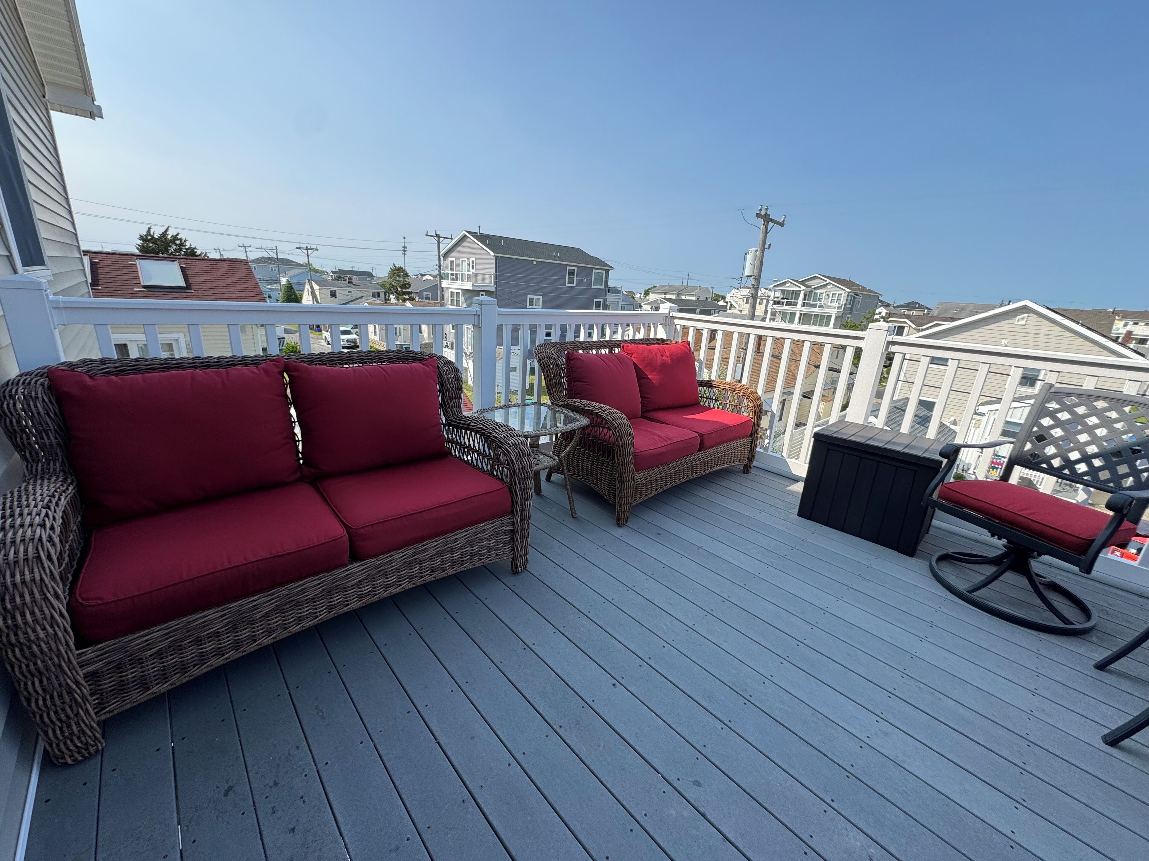 Eine überdachte Terrasse im Freien mit Rattanmöbeln und Blick auf benachbarte Häuser.