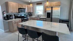 Una cocina moderna con una isla grande, armarios de madera, electrodomésticos de acero inoxidable e iluminación colgante.