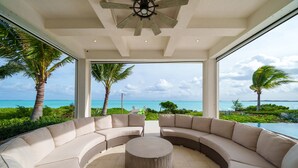 Un espace extérieur moderne, aménagé avec un canapé incurvé et une table ronde centrale, offrant une vue imprenable sur l’océan.