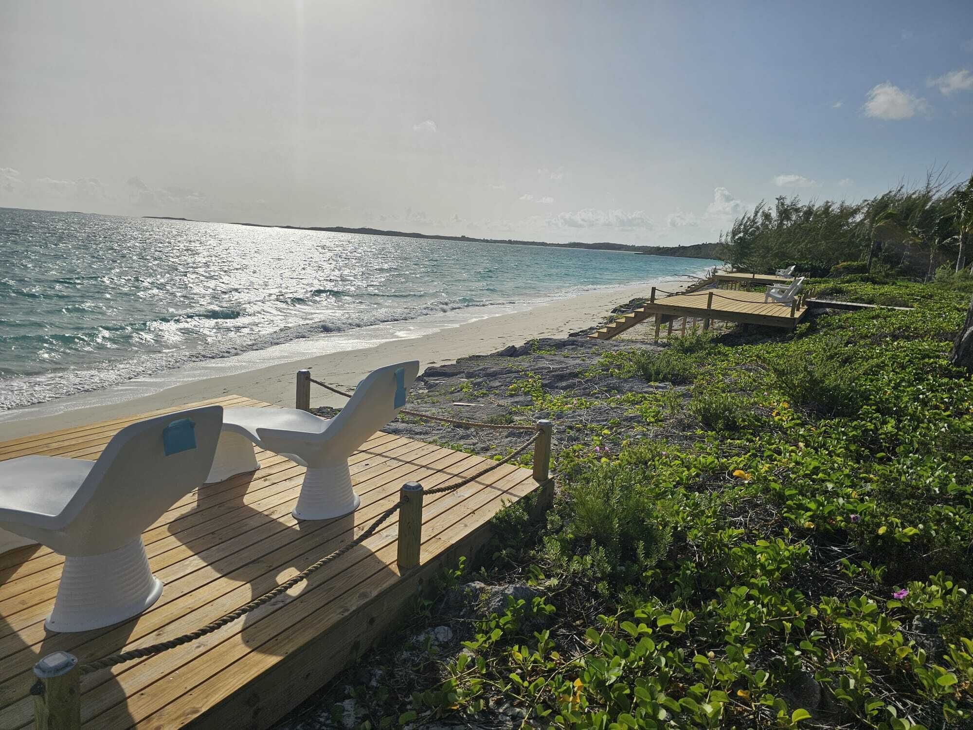 A wooden deck with two white chairs facing the ocean.