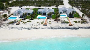 Une propriété située en bord de mer, comprenant plusieurs maisons, une piscine et une plage de sable.