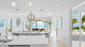 Une cuisine moderne dotée d’un îlot central, un coin repas offrant une vue sur l’océan et un salon avec une grande fenêtre donnant sur la plage.